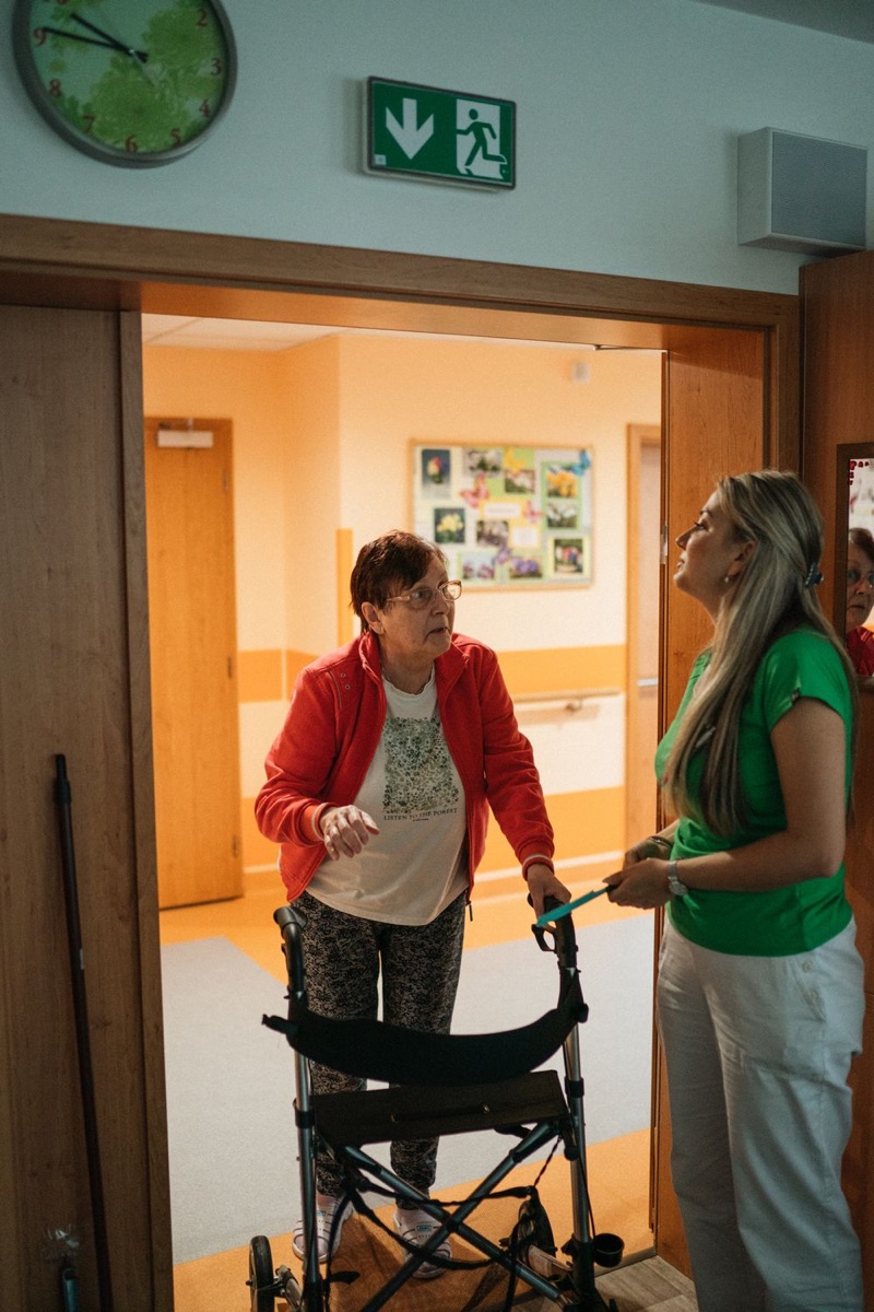Caregiver assisting an older woman using a walker in a residential care corridor